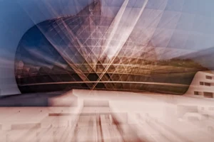 Cette photographie capture un sujet flou en mouvement rapide, probablement un véhicule ou un objet métallique. La composition met en avant des lignes dynamiques et des traînées lumineuses, créant un effet de vitesse et d'abstraction. Le cadrage est serré, centré sur ces éléments, avec un arrière-plan légèrement visible mais flouté.La lumière est douce et diffuse, avec des reflets et des éclats blancs. Les couleurs dominantes sont des teintes froides et métalliques, avec des touches de gris et de bleu pâle. Le style est artistique et expérimental, évoquant une ambiance moderne et futuriste, presque onirique.