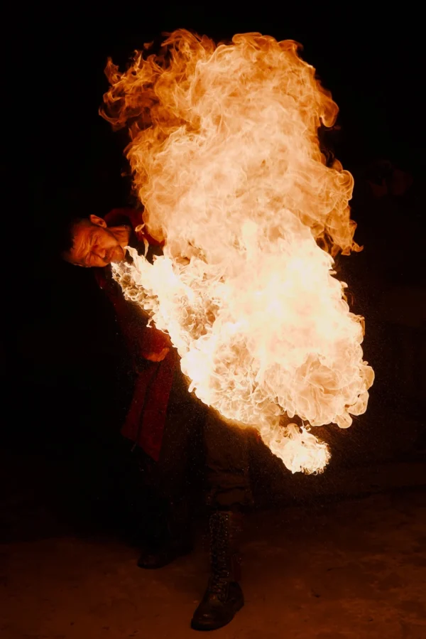 Frédéric · 1121 x 1680 Cette photographie met en scène un **sujet principal** : un performer manipulant une **grosse boule de feu**. La **composition** est épurée, centrée sur l’effet pyrotechnique. Le **cadrage** est serré, isolant le feu et le bras du performer dans l’obscurité.La **lumière** est dramatique, avec une **couleur dominante** orange-jaune intense, contrastant avec le fond noir. Le **style** est réaliste et dynamique, évoquant une performance artistique ou un spectacle. L’**ambiance** est spectaculaire, presque mystique, soulignant la puissance et le danger du feu.