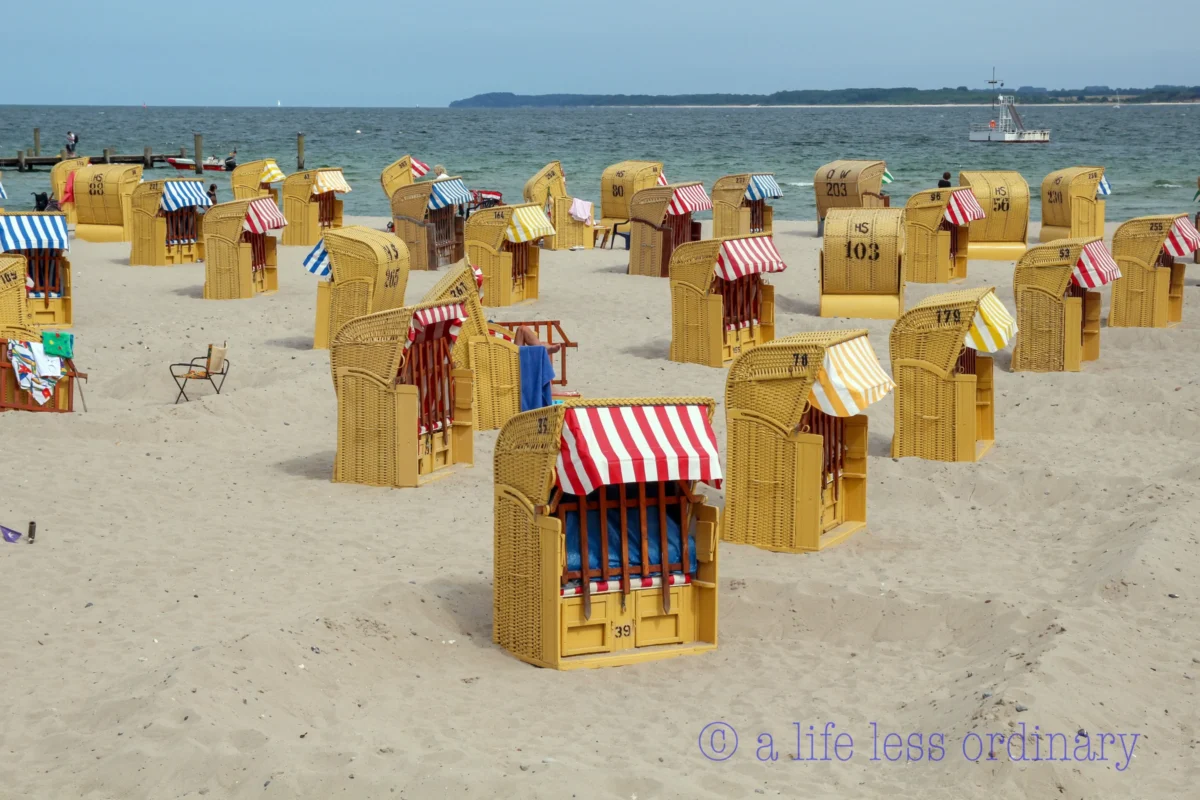 Cédric · 07/08/2013 · 5157 x 3438 Cette photographie montre une plage avec des **chaise-longues de plage en bois** comme sujet principal. La composition est symétrique, avec des rangées de transats alignées sur le sable.Le cadrage est large, incluant l’horizon marin. La lumière est naturelle et éclatante, typique d’un jour ensoleillé. Les couleurs dominantes sont les **tons chauds (beige, jaune des transats)** et les **accents vifs (rouge et bleu des coussins)**.Le style est documentaire et estival, évoquant une ambiance **détendue et balnéaire**, propice aux vacances.