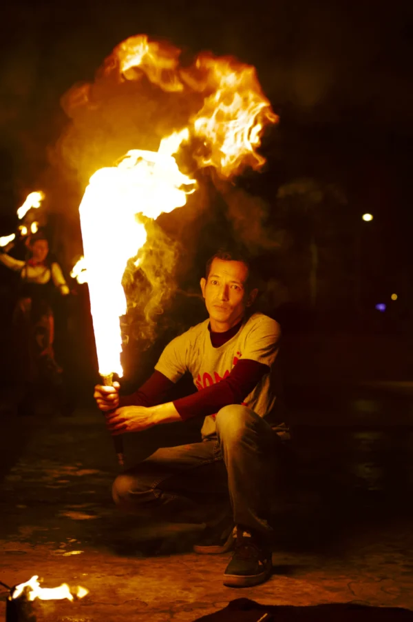Thomas · 24/01/2026 · 2048 x 3080 Cette photographie met en scène un homme comme sujet principal, assis près d’un feu spectaculaire. La composition est centrée sur lui, avec une flamme imposante en arrière-plan, créant un contraste saisissant. Le cadrage est serré, mettant en valeur les expressions et l'action.Les lumières chaudes dominent, avec des teintes orangées et jaunes, accentuant l’ambiance dramatique. Les couleurs froides sont quasi absentes, renforçant l’effet de chaleur intense. Le style est réaliste et dynamique, évoquant une scène de spectacle ou d’art de rue. L’ambiance est à la fois mystérieuse et captivante, mêlant danger et fascination.