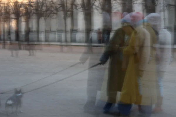 Laurence · 3472 x 2320 Cette photographie présente une scène floue et légèrement surexposée, donnant un effet onirique. Le sujet principal semble être un groupe de personnes, dont une en jaune, avec un chien en bas à gauche. La composition est dynamique, avec des formes indistinctes suggérant un mouvement.Le cadrage est large, incluant un espace ouvert et des arbres en arrière-plan. La lumière est douce et diffuse, créant une ambiance tamisée et froide. Les couleurs dominantes sont des tons gris-beige, avec des touches de jaune et de bleu pâle. Le style est artistique, presque abstrait, évoquant une atmosphère mystérieuse et poétique.