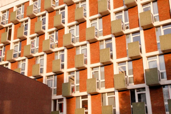 Cédric · 17/01/2026 · 2048 x 1365 Cette photographie montre un immeuble résidentiel moderne. Le sujet principal est la façade aux balcons en saillie, alignés de manière géométrique. La composition est symétrique et répétitive, avec un cadrage serré mettant en valeur les détails architecturaux.Les couleurs dominantes sont des tons orangés et bruns, adoucis par des balcons verts et blancs. La lumière naturelle, probablement en fin de journée, crée des ombres douces et accentue les contrastes.Le style est épuré et contemporain, évoquant une ambiance urbaine et moderne, à la fois chaleureuse et structurée.