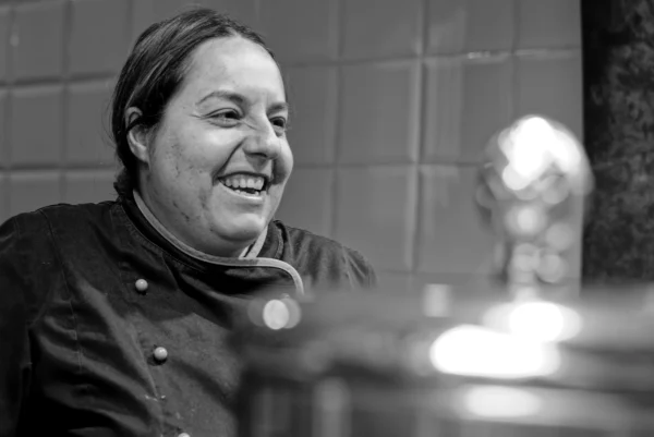Mickaël · 10/01/2026 · 4592 x 3066 Cette photographie en noir et blanc met en scène une personne souriante, probablement un cuisinier, vêtue d'une tenue professionnelle. Le sujet principal est centré, avec un cadrage serré qui isole son visage et ses épaules.L'arrière-plan montre une partie de cuisine avec des carreaux et un ustensile, suggérant un environnement professionnel. La lumière est douce et naturelle, éclairant le visage de manière homogène. L'ambiance est chaleureuse et conviviale, renforcée par le sourire du sujet. Le style est simple et direct, mettant l'accent sur l'authenticité et l'émotion.