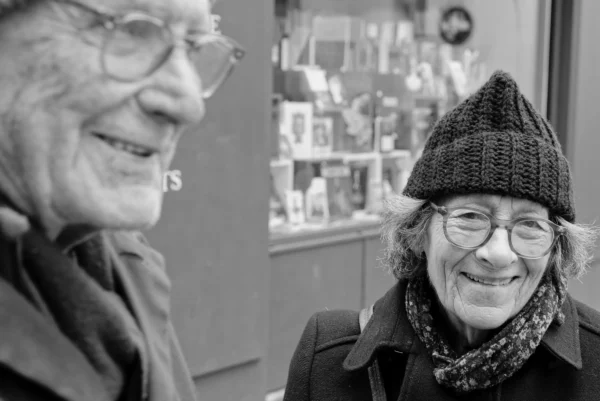 Mickaël · 10/01/2026 · 3666 x 2447 Cette photographie en noir et blanc met en scène deux personnes âgées souriantes, formant le sujet principal. La composition est serrée, centrée sur leurs visages, créant une intimité. Le cadrage est rapproché, mettant l'accent sur leurs expressions joyeuses.La lumière est douce et naturelle, éclairant leurs traits sans ombres marquées. Les couleurs, bien que monochromes, jouent sur les contrastes de gris et de noirs, renforçant les détails des visages et des textures.Le style est documentaire et chaleureux, évoquant une ambiance conviviale et humaine.