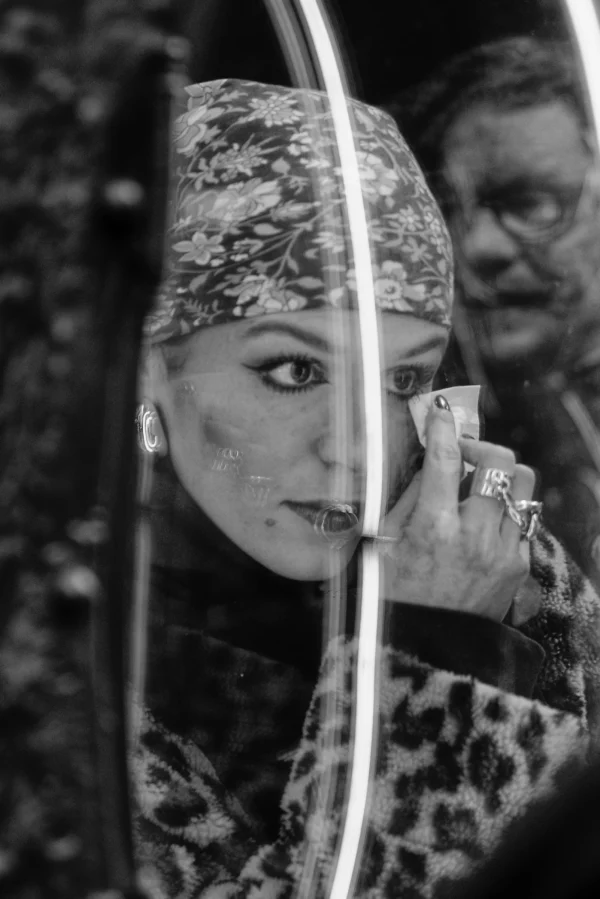 Mickaël · 10/01/2026 · 1919 x 2875 Cette photographie en noir et blanc met en scène une femme comme sujet principal, vue de profil. Elle semble appliquer du maquillage devant un miroir.La composition est serrée, avec un cadrage qui isole son visage et ses mains. Un fil métallique traverse l’image, ajoutant une touche graphique. La lumière est douce, mettant en valeur les traits délicats de son visage. L’ambiance est intime et légèrement mélancolique, renforcée par les contrastes des ombres et lumières.Le style est artistique et minimaliste, typique d’une approche documentaire ou conceptuelle.
