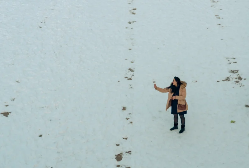 Don · 4714 x 3195 Cette photographie montre une personne en mouvement dans un paysage enneigé, vêtue d’un manteau orange et d’un bonnet sombre. Le sujet principal est isolé, au centre, avec des traces de pas dans la neige.Le cadrage est serré et aérien, comme pris depuis une hauteur. La composition est épurée, mettant en valeur la solitude et l’immensité de l’environnement. La lumière semble douce et naturelle, sans contraste marqué.Les couleurs dominantes sont le blanc de la neige, l’orange du manteau et les tons froids du paysage. Le style est documentaire et sobre, évoquant une ambiance calme et contemplative, presque mélancolique.