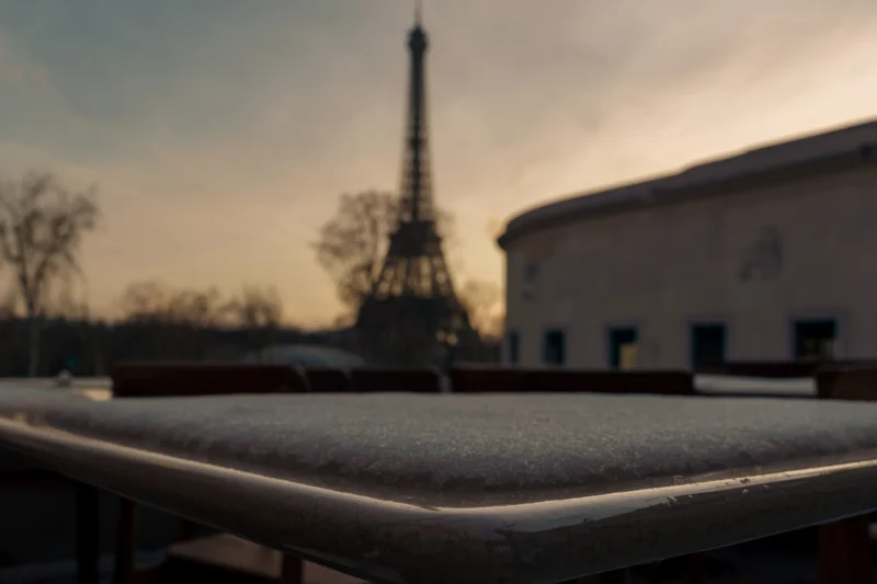 Don · 5235 x 3490 Cette photographie met en scène la silhouette floue de la **Tour Eiffel** en arrière-plan. Le **sujet principal** semble être une surface métallique en premier plan, probablement un toit ou une rambarde, légèrement mouillée ou couverte de givre.La **composition** joue sur les contrastes entre premier et arrière-plan. Le **cadrage** est serré, avec une profondeur de champ réduite, créant un effet bokeh. La **lumière** est douce, probablement crépusculaire, adoucissant les contours. Les **couleurs dominantes** sont des tons froids (bleutés, gris) avec des touches de jaune pâle.Le **style** est esthétique et poétique, évoquant une **ambiance** mélancolique et onirique.
