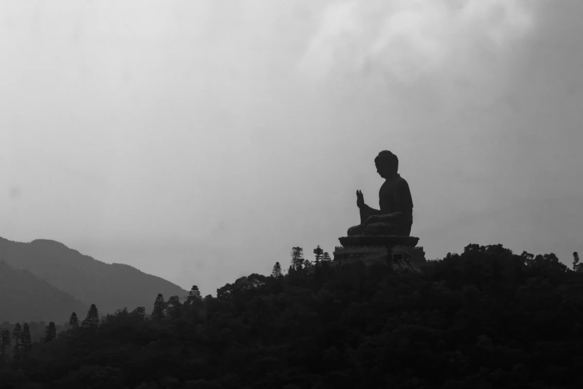 Daniel · 28/09/2019 · 4628 x 3085 Cette photographie en noir et blanc met en scène un **statue bouddhiste** assise en méditation, sujet principal. La **composition** est épurée, avec la statue en silhouette sur une colline, entourée de formes floues suggérant des arbres et des montagnes.Le **cadrage** est serré sur la statue, isolée et dominant le paysage. La **lumière** douce et diffuse crée un contraste entre les ombres et les zones éclairées, accentuant la sérénité. Les **couleurs dominantes** sont les nuances de gris, renforçant l'atmosphère contemplative.Le **style** est minimaliste et poétique, évoquant une **ambiance** de paix et de spiritualité, typique des lieux sacrés.
