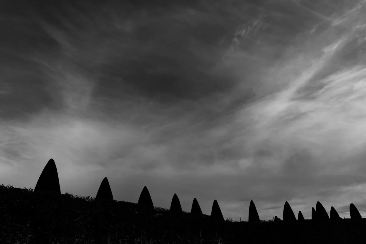 Daniel · 12/10/2015 · 4188 x 2795 Cette photographie en noir et blanc met en scène une série de toits coniques, probablement ceux d’une région comme la Toscane ou la Provence. La composition repose sur une répétition rythmée de ces formes, alignées en perspective convergente.Le cadrage est serré, centré sur les toits avec un ciel dramatique en arrière-plan. La lumière, contrastée, accentue les ombres et les contours, créant une ambiance mystérieuse et presque dramatique. Les teintes dominantes, en niveaux de gris, renforcent l’atmosphère contemplative et intemporelle, évoquant sérénité et mélancolie. Le style est épuré et minimaliste.
