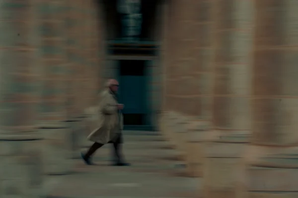 Don · 6085 x 4057 Cette photographie montre une personne floue en mouvement, vêtue d'un long manteau clair, traversant un couloir ou une allée étroite bordée de murs en pierre.Le cadrage est serré, centré sur le sujet. La lumière est tamisée, créant une ambiance sombre et mystérieuse. Les couleurs dominantes sont des tons froids et terreux, avec des gris et des bruns.Le style évoque un flou artistique, peut-être lié à un mouvement rapide ou à une technique volontaire. L’ambiance générale est mélancolique et onirique.