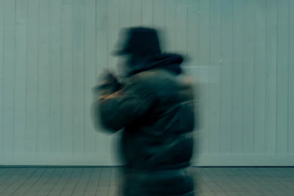 Don · 6226 x 4151 Cette photographie montre un sujet principal flou, probablement une personne en mouvement, vêtue d'une veste épaisse et d'un chapeau. La composition est simple, avec un cadrage serré centré sur le personnage. La lumière est douce et diffuse, créant une ambiance tamisée et peu contrastée. Les couleurs dominantes sont des teintes froides et grises, avec des nuances bleutées sur le fond.Le style est minimaliste et abstrait, renforcé par le flou de mouvement. L'ambiance évoque mystère et dynamisme, presque onirique.