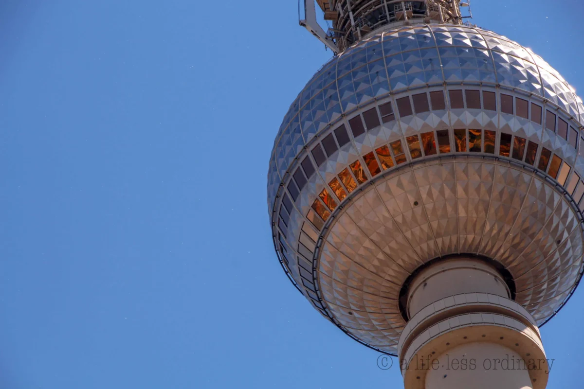 Cédric · 27/05/2017 · 5184 x 3456 Cette photographie met en scène le **Fernsehturm de Berlin**, tour emblématique. Le **sujet principal** est le globe métallique et sa base élancée, cadrés en **gros plan depuis le bas**, accentuant sa hauteur.La **composition** est épurée, centrée sur la structure. La **lumière** naturelle, douce et légèrement dorée, souligne les détails architecturaux. Les **couleurs dominantes** sont le **bleu clair du ciel** et les teintes **métalliques grises et orangées** de la tour.Le style est **minimaliste et moderne**, créant une **ambiance futuriste et monumentale**.
