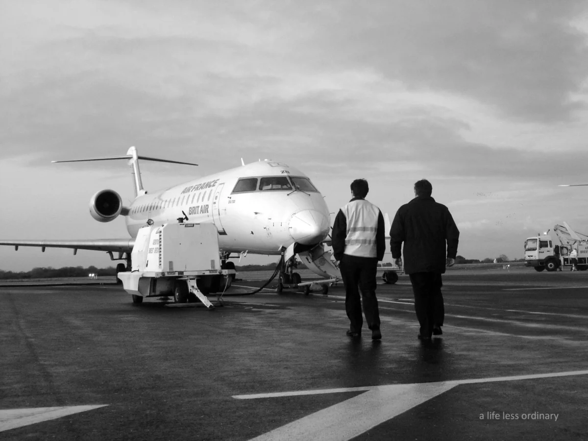 Cédric · 02/01/2007 · 2592 x 1944 Cette photographie en noir et blanc montre deux hommes en tenue professionnelle marchant vers un avion régional. Le sujet principal est l'avion et les deux individus, soulignant une scène aéroportuaire.La composition est équilibrée, avec les personnages au premier plan et l'avion en arrière-plan. Le cadrage est large, capturant une partie de la piste et du tarmac. La lumière est diffuse, typique d'un jour nuageux, adoucissant les contrastes. Les couleurs dominantes, bien que monochromes, suggèrent des tons gris et blancs, renforçant une ambiance sobre et professionnelle. Le style est documentaire, reflétant une réalité industrielle. L'ambiance est calme et fonctionnelle.