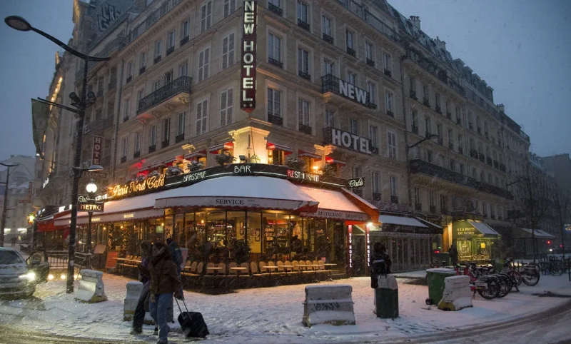 Franck T. · 07/01/2026 · 1400 x 844 Cette photographie met en scène un **café-restaurant parisien** sous la neige, avec son **auvent éclairé** comme sujet principal. La composition montre une **rue urbaine animée**, avec des bâtiments anciens en arrière-plan.Le **cadrage** est serré sur l’établissement, captant son ambiance chaleureuse malgré le froid. La **lumière** est douce et artificielle, provenant des éclairages chauds du café, contrastant avec la nuit hivernale.Les **couleurs dominantes** sont les tons froids (blanc de la neige, gris des bâtiments) et les **lueurs chaudes** (jaunes et oranges des vitrines). Le style est **urbain et intimiste**, évoquant une **ambiance romantique et paisible**.