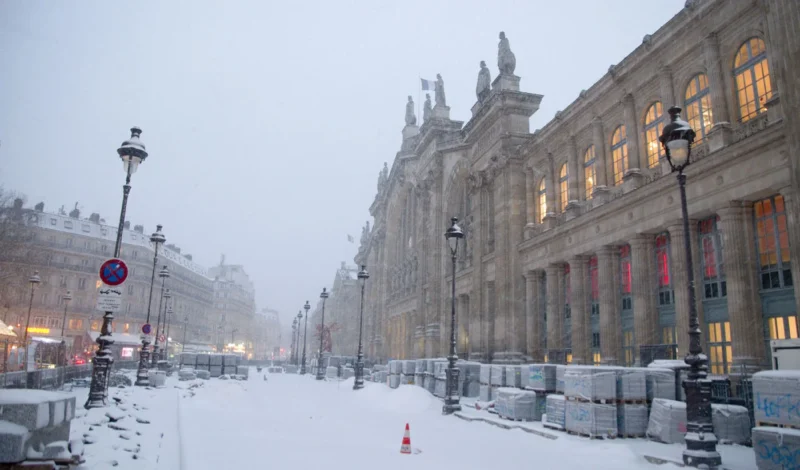 Franck T. · 07/01/2026 · 1400 x 822 Cette photographie capture une rue parisienne enneigée. Le sujet principal est l’architecture classique d’un bâtiment imposant, probablement une gare, avec ses colonnes et sa façade ornées.La composition montre une perspective symétrique, avec la voie centrale bordée de neige et de lampadaires. Le cadrage est serré, mettant en valeur les détails architecturaux et l’ambiance hivernale.La lumière est tamisée, créant une atmosphère douce et froide. Les couleurs dominantes sont les tons gris-beige de la neige et des bâtiments, adoucis par les éclairages jaunâtres des lampadaires.Le style est réaliste et atmosphérique, évoquant une ambiance calme et nostalgique.