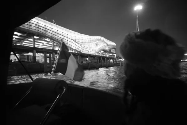 Thierry · 08/01/2026 · 3840 x 2560 Cette photographie en noir et blanc capture un moment sur un bateau. Le sujet principal semble être une personne dont on ne voit que le profil, tournée vers la droite.La composition montre un cadrage serré avec une perspective depuis l'intérieur du bateau, mettant en avant l'eau agitée et une structure lumineuse en arrière-plan, probablement un port ou une jetée. La lumière est douce mais contrastée, créant des ombres marquées. Les couleurs dominantes, bien que monochromes, jouent sur les nuances de gris et de noir, renforçant une ambiance nocturne et mystérieuse. Le style est documentaire et intimiste, évoquant une sensation de mouvement et de solitude.