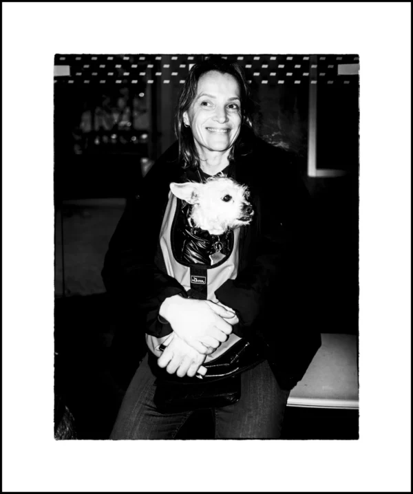 Thierry · 22/02/2026 · 3912 x 4680 Cette photographie en noir et blanc met en scène une femme souriante, sujet principal, tenant un chaton dans ses bras. La composition est simple et centrée, avec un cadrage serré sur elle. L’arrière-plan flou suggère un intérieur lumineux, probablement un bar ou un restaurant.La lumière est douce et naturelle, mettant en valeur les traits de la femme et créant des contrastes subtils. Les couleurs dominantes sont les nuances de gris, typiques du noir et blanc, renforçant l’ambiance chaleureuse et intime. Le style est spontané et authentique, évoquant une scène du quotidien. L’ambiance est conviviale et tendre.