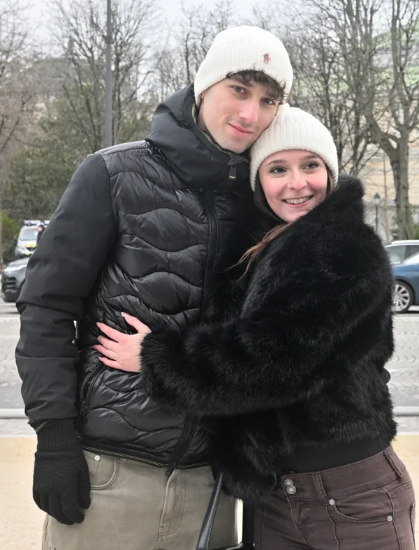 Mary · 14/02/2026 · 2120 x 2784 Cette photographie montre deux jeunes posant ensemble. Le sujet principal est un couple souriant, l’un vêtu d’une veste noire matelassée et l’autre d’un manteau à fourrure noire avec un béret blanc. Le cadrage est serré, centré sur eux, avec un arrière-plan flou de voitures et d’arbres.La lumière semble naturelle, probablement en journée. Les couleurs dominantes sont les tons froids (noir, gris) et quelques touches chaudes (fourrure, peau). Le style est décontracté et spontané, évoquant une ambiance conviviale et hivernale.