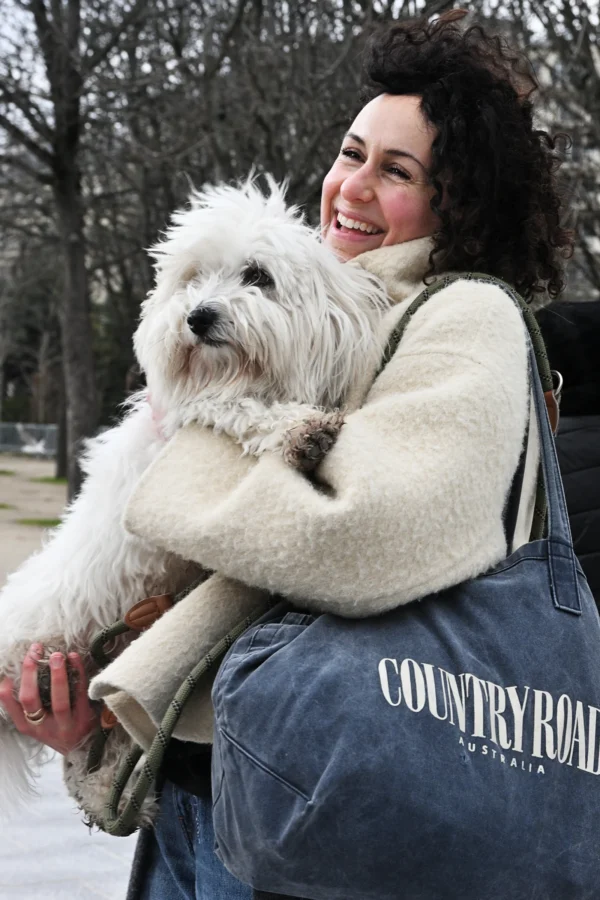Mary · 14/02/2026 · 1856 x 2784 Cette photographie met en scène une femme souriante tenant un petit chien blanc dans ses bras. Le sujet principal est la complicité entre la femme et son animal.La composition est simple et centrée, avec un cadrage serré sur les deux sujets. La lumière naturelle semble douce, éclairant légèrement les visages et le chien. Les couleurs dominantes sont les tons neutres (beige, gris) et blancs, adoucis par les teintes naturelles du parc en arrière-plan.Le style est naturel et spontané, évoquant une ambiance chaleureuse et apaisante.