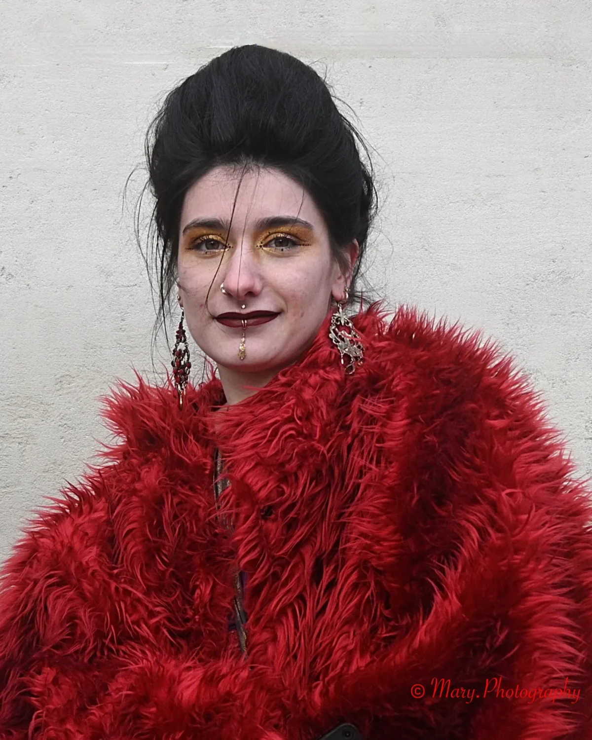 Mary · 2227 x 2784 Cette photographie met en scène une personne comme sujet principal, vêtue d’un manteau en fourrure rouge vif. Le cadrage est serré, centré sur son visage et sa tenue.La lumière semble naturelle, douce et légèrement contrastée, mettant en valeur les traits du visage et les détails du manteau. Les couleurs dominantes sont le rouge intense de la fourrure et les tons neutres du fond.Le style évoque un côté théâtral et vintage, renforcé par le maquillage et la coiffure sophistiqués. L’ambiance est à la fois mystérieuse et élégante, avec une touche de dramatisme.