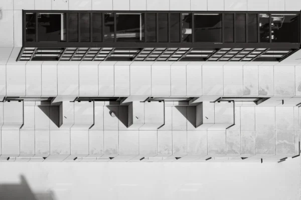 Jean-Marc · 21/02/2026 · 3909 x 2606 Cette photographie en noir et blanc montre des **toilettes publiques** urbaines en sujet principal. La composition met en avant des rangées de cabines alignées sous une structure architecturale moderne.Le **cadrage** est serré, centré sur les urinoirs et les parois lisses. La lumière est naturelle, contrastée, créant des ombres marquées. Les **couleurs dominantes** sont les tons de gris, renforçant un style épuré et contemporain.L’ambiance est **minimaliste et aseptisée**, évoquant une froideur fonctionnelle, typique des espaces publics modernes.