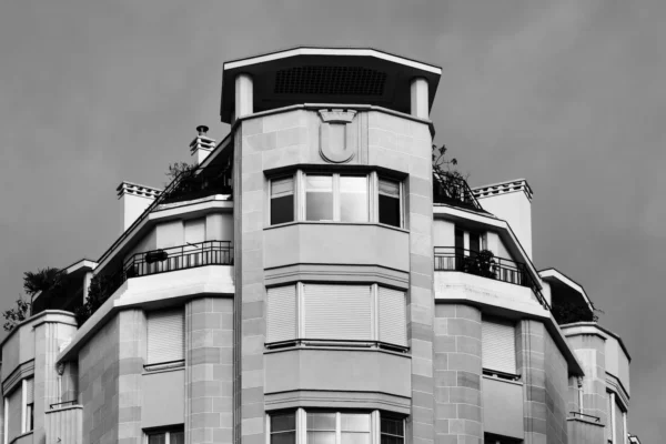 Xavier · 1600 x 1067 Cette photographie met en scène un immeuble Art déco aux lignes élégantes et arrondies. Le sujet principal est ce bâtiment, capturé en gros plan depuis le bas, avec une composition verticale accentuant sa hauteur.Le cadrage serré isole la structure, mettant en valeur ses détails architecturaux. La lumière, douce et uniforme, crée des contrastes subtils en noir et blanc, soulignant les textures et les formes géométriques. Les tons dominants sont les gris et les noirs, renforçant l'ambiance sobre et intemporelle.Le style rappelle l’architecture des années 1920-1930, évoquant une élégance rétro et une atmosphère à la fois moderne et nostalgique.