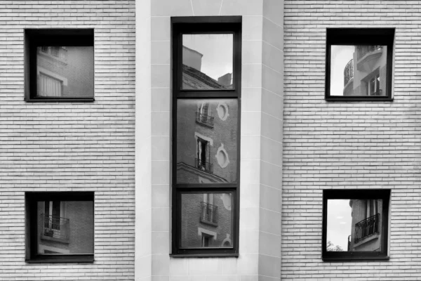 Xavier · 1600 x 1067 Cette photographie en noir et blanc met en scène une façade d’immeuble avec trois fenêtres verticales alignées. Le sujet principal est la réflexion et la superposition des images à travers ces fenêtres, créant un effet de miroir et de profondeur.La composition repose sur une symétrie et un cadrage serré, mettant en valeur les jeux de perspectives et les reflets. La lumière, douce et naturelle, accentue les contrastes et les ombres, renforçant l’aspect graphique. Les couleurs dominantes, bien que monochromes, jouent sur les nuances de gris.Le style est épuré et artistique, évoquant une ambiance à la fois moderne et intemporelle, presque onirique.
