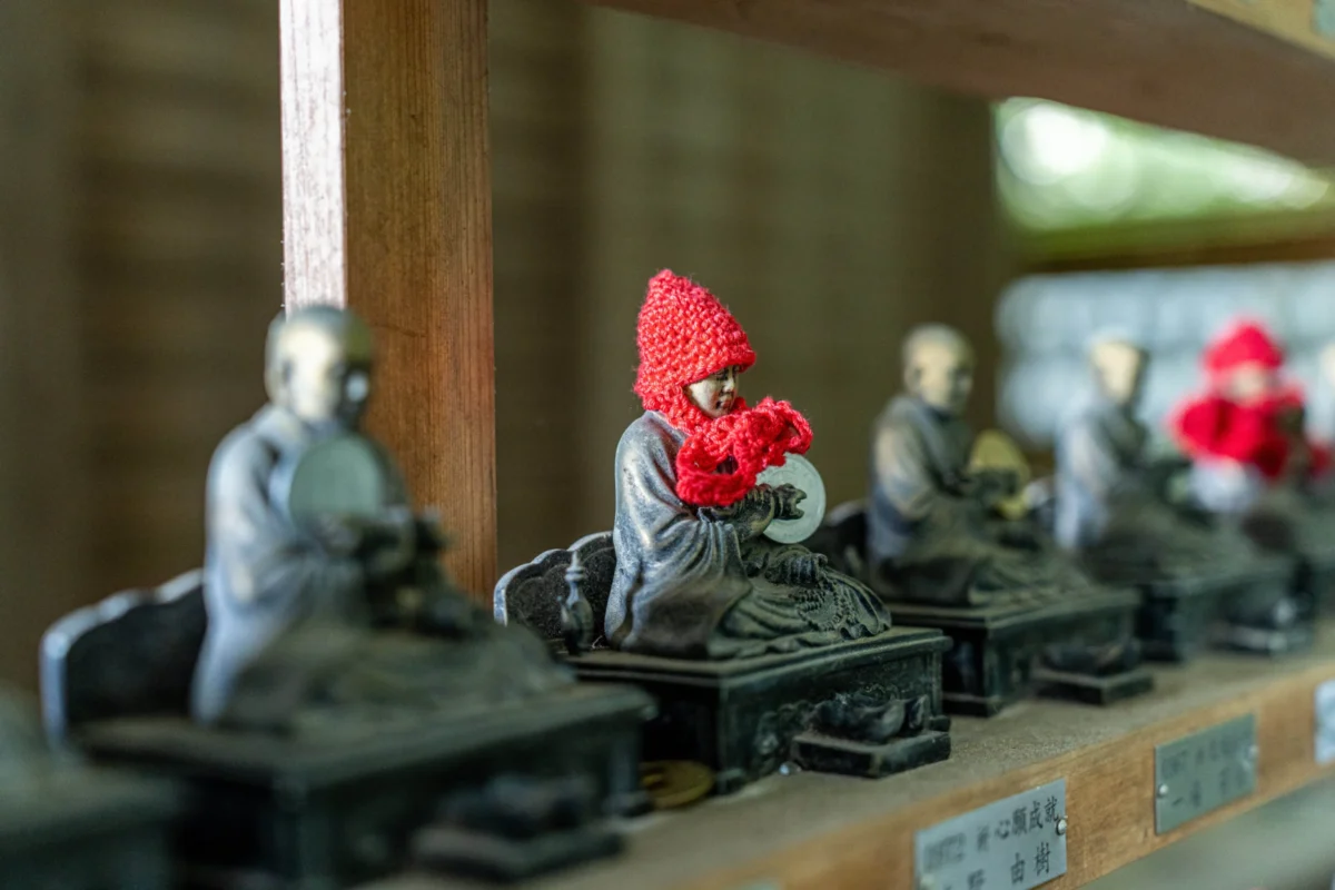 Marc · 21/04/2025 · 7008 x 4672 Cette photographie montre des figurines en métal représentant des samouraïs, disposées sur des socles en bois. Le sujet principal est un samouraï avec un casque rouge, mis en valeur par un cadrage serré.La composition est horizontale, avec plusieurs figurines alignées sur une étagère en bois. La lumière naturelle, douce et légèrement tamisée, accentue les détails et crée des ombres douces. Les couleurs dominantes sont les tons gris métalliques des figurines, contrastés par les rouges vifs des casques et le bois naturel.L’ambiance est à la fois traditionnelle et contemplative, évoquant un style artisanal et historique.