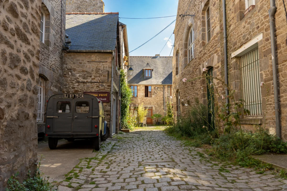 Marc · 21/08/2023 · 7008 x 4672 Cette photographie montre une **ruelle pavée étroite** dans un village ancien. Le **sujet principal** est l’allée bordée de **maisons en pierre**, avec un **véhicule ancien** garé sur la gauche.La **composition** est symétrique et profonde, guidant le regard vers l’horizon. Le **cadrage** est serré, mettant en valeur les détails architecturaux. La **lumière** est naturelle, douce et légèrement dorée, créant des ombres douces.Les **couleurs dominantes** sont les **tons gris-beige** des pierres, avec des touches de **vert** (végétation) et **bleu clair** (ciel). Le style évoque un **paysage rural traditionnel**, tandis que l’ambiance est **calme et nostalgique**, presque intemporelle.