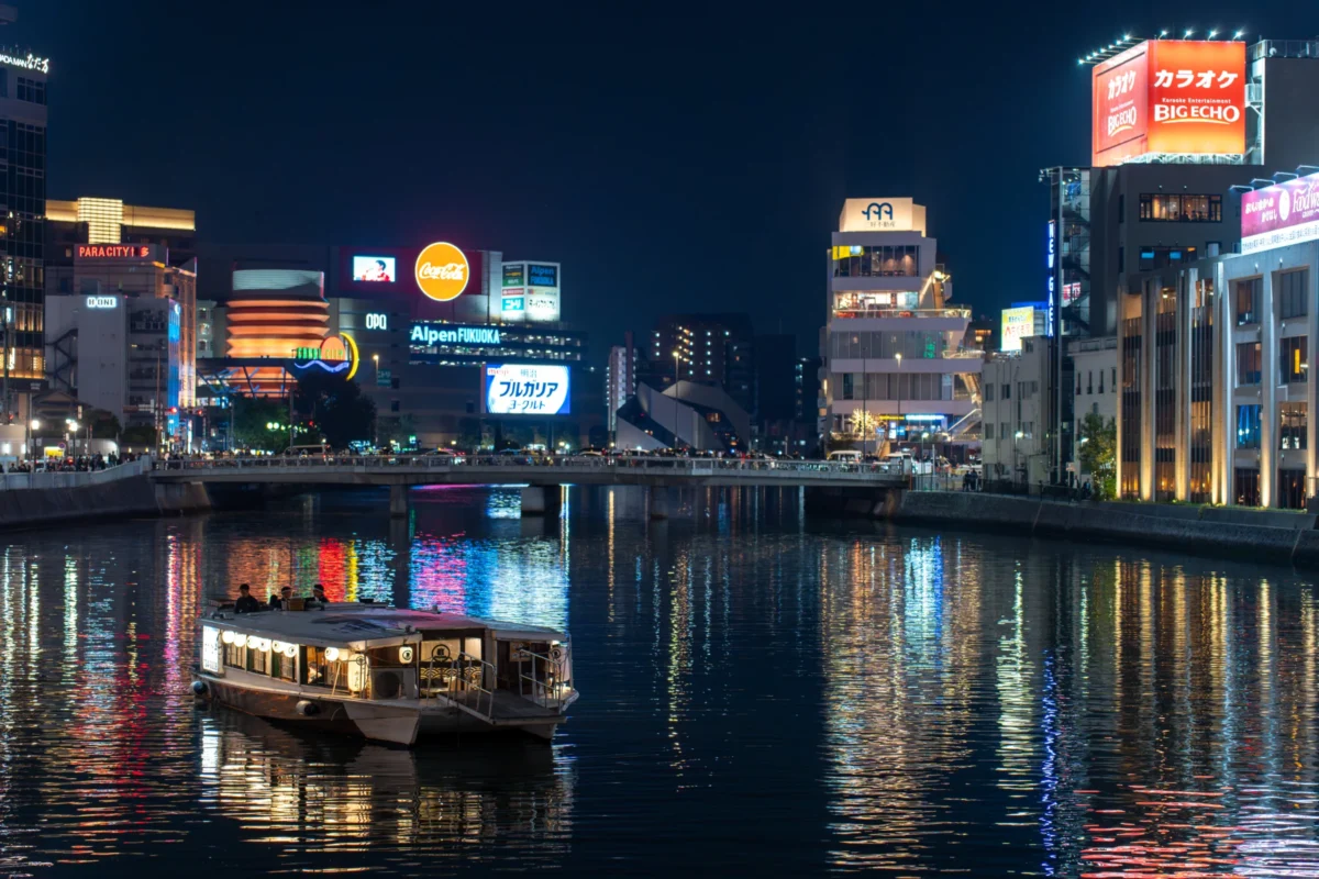 Marc · 25/04/2025 · 6805 x 4537 Cette photographie capture une ville nocturne illuminée, avec un bateau comme sujet principal sur un plan d’eau calme. La composition montre une perspective symétrique, reflétant les lumières des buildings dans l’eau. Le cadrage est large, incluant un horizon urbain dense.Les couleurs dominantes sont des teintes vives et froides : bleus, violets, jaunes néon et blancs lumineux. La lumière est artificielle, créant une ambiance dynamique et moderne. Le style est photographique urbain, mettant en valeur l’architecture nocturne et l’animation nocturne. L’ambiance est à la fois vibrante et sereine, mêlant énergie et tranquillité.