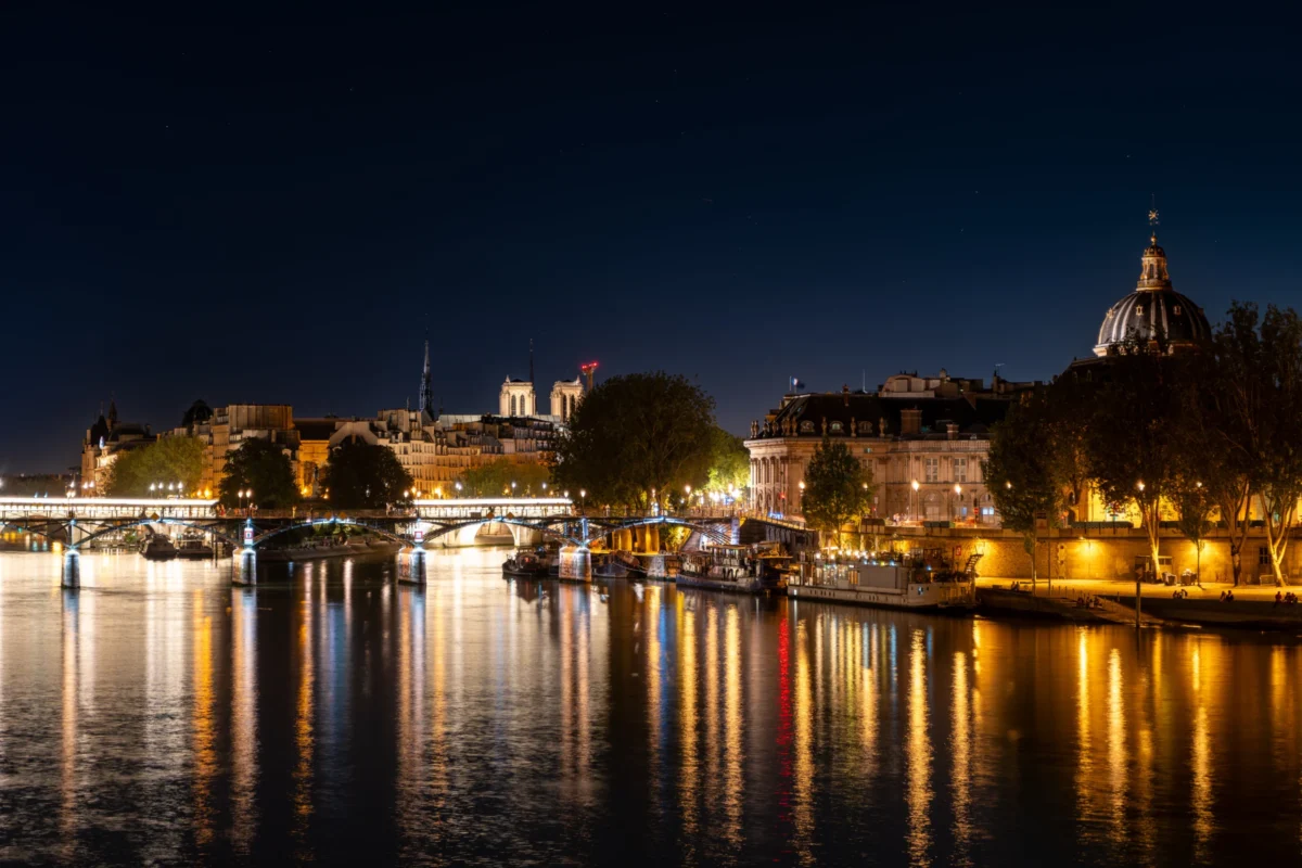 Marc · 11/08/2024 · 7008 x 4672 Cette photographie capture un **pont illuminé de nuit** sur une rivière, reflétant les lumières dans l’eau. Le **sujet principal** est le **pont et ses abords**, avec des bâtiments historiques en arrière-plan.La **composition** est équilibrée, avec une perspective symétrique et des jeux de reflets. Le **cadrage** est large, englobant le paysage urbain nocturne. Les **lumières chaudes** dominent, créant une ambiance douce et contrastée avec le ciel sombre. Les **couleurs** sont principalement des tons **jaunes, ors et bleus nocturnes**.Le **style** est photographique réaliste, mettant en valeur une **ambiance poétique et sereine**, typique des villes européennes la nuit.