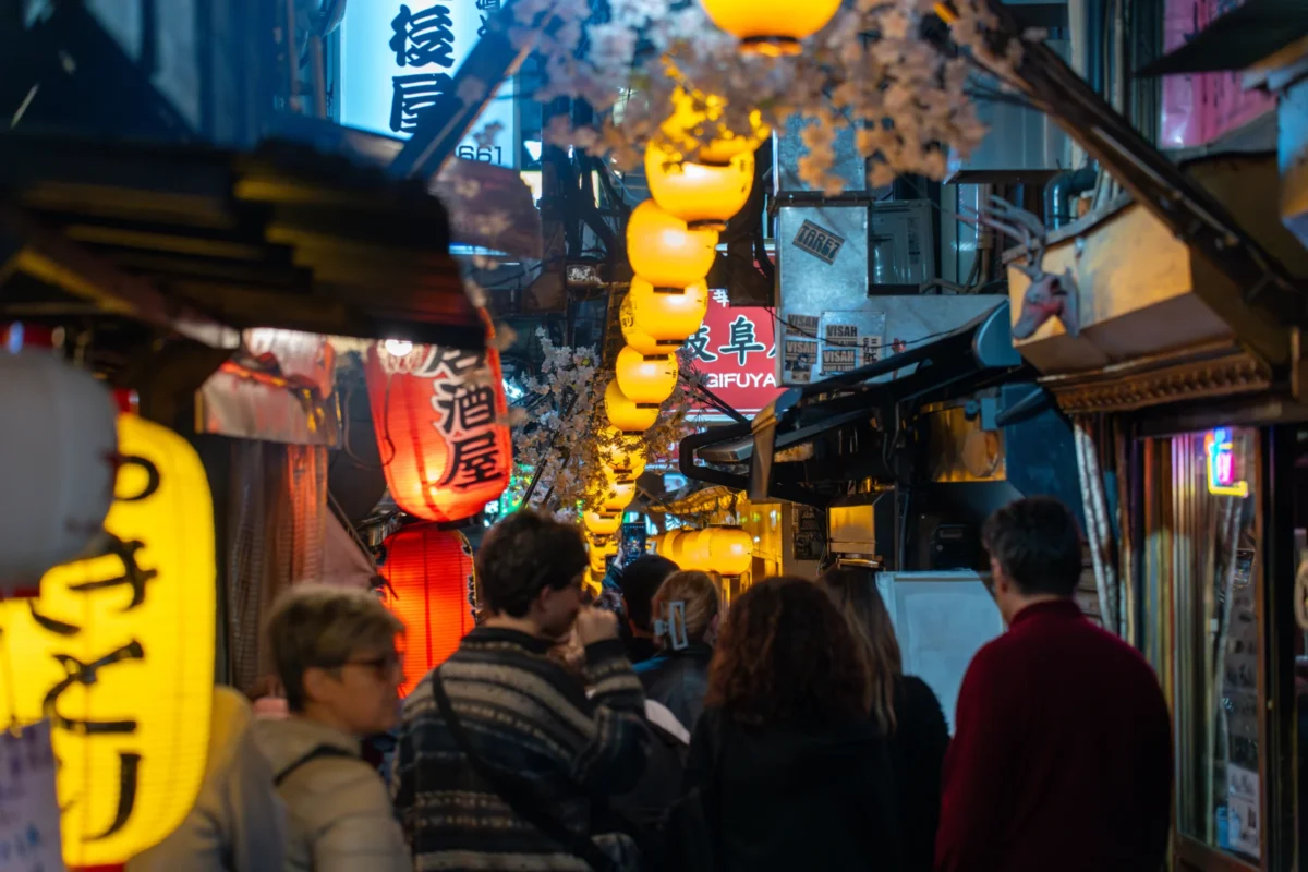 Marc · 16/04/2025 · 7008 x 4672 Cette photographie capture une rue animée, probablement asiatique, de nuit. Le sujet principal est une foule de personnes en mouvement, éclairées par des enseignes lumineuses colorées.La composition met en avant des lanternes jaunes et des guirlandes lumineuses, créant un cadrage dynamique et serré. Les couleurs dominantes sont les tons chauds (jaune, orange) et les néons vifs.Le style est urbain et festif, évoquant une ambiance nocturne vivante et animée, typique des marchés ou quartiers commerçants traditionnels. La lumière artificielle accentue l'atmosphère chaleureuse et festive.