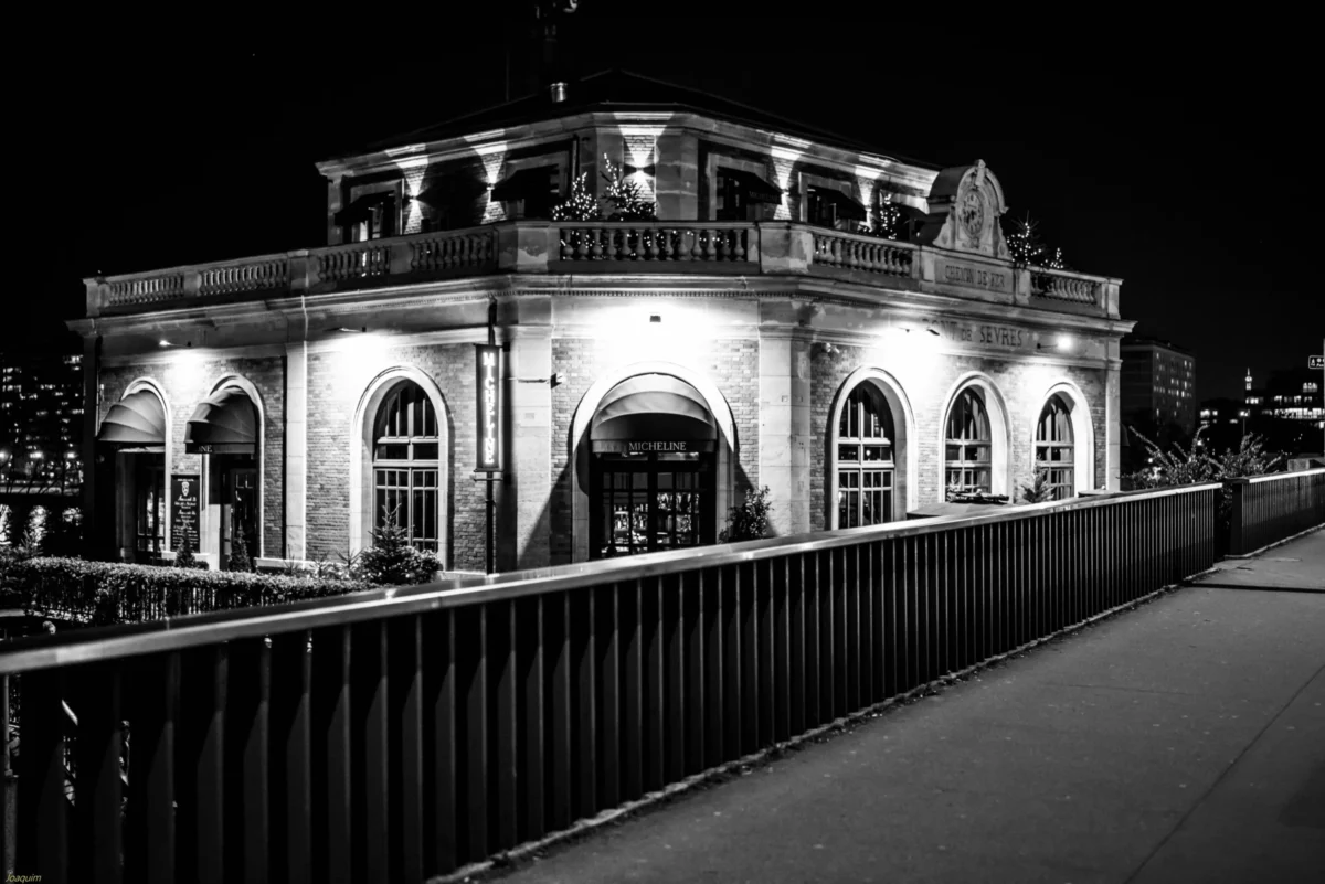 Pierre-Joaquim · 01/01/2014 · 7360 x 4912 Cette photographie montre un bâtiment historique éclairé la nuit, probablement une gare ou un édifice public, avec l'inscription "Südbahnhof". Le sujet principal est l’architecture élégante, soulignée par des arcs et des balcons.La composition est symétrique, avec un cadrage serré sur le bâtiment. La lumière, douce et contrastée, met en valeur les détails architecturaux. Les couleurs dominantes sont les tons de gris et noir, typiques d’une photo en noir et blanc, renforçant l’ambiance nocturne et mystérieuse. Le style est classique et intemporel, évoquant une atmosphère calme et élégante.