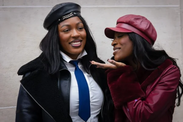 Claude · 1080 x 720 Cette photographie met en scène deux femmes souriantes, formant le sujet principal. La composition est serrée, centrée sur leurs visages et expressions joyeuses. Le cadrage est rapproché, créant une ambiance intime.La lumière semble naturelle et douce, éclairant leurs traits sans ombres marquées. Les couleurs dominantes sont vives : le bleu et le noir pour la tenue de la femme à gauche, et le rouge pour celle à droite, avec un fond neutre grisâtre.Le style est spontané et décontracté, évoquant une ambiance amicale et chaleureuse.