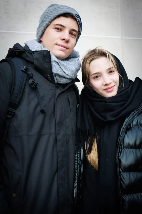 Claude · 900 x 1350 Cette photographie met en scène deux jeunes posant côte à côte. Le sujet principal est leur complicité et leur proximité. La composition est symétrique, avec un cadrage serré sur leurs visages et épaules.La lumière est douce et naturelle, légèrement tamisée, créant des ombres subtiles. Les couleurs dominantes sont les tons froids : gris, noir et bleu foncé, adoucis par des touches de gris clair et de beige.Le style est simple et spontané, évoquant une ambiance authentique et chaleureuse malgré le froid.