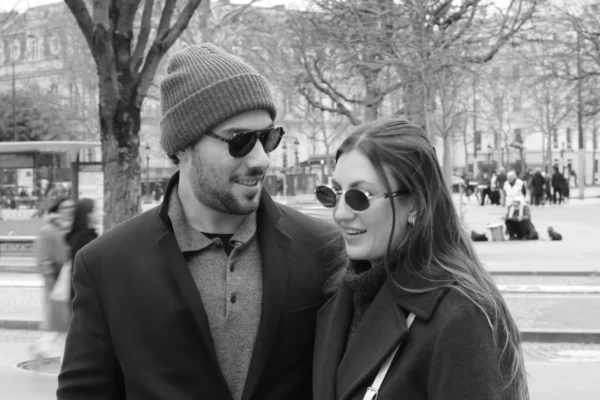 Vera · 6960 x 4640 Cette photographie en noir et blanc met en scène un couple comme sujet principal. Le cadrage est serré sur eux, avec un fond flou montrant une place publique animée.La composition est symétrique et intime, avec les deux personnages proches. La lumière semble naturelle, douce et légèrement contrastée, mettant en valeur leurs traits. Les couleurs dominantes, bien que monochromes, jouent sur les nuances de gris, avec des détails légèrement plus clairs pour les visages et les vêtements.Le style est sobre et élégant, évoquant une ambiance romantique et chaleureuse.
