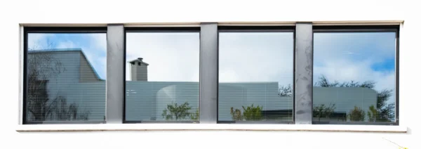 Alice · 21/02/2026 · 6351 x 2247 Cette photographie montre une vue reflétée à travers une série de vitres, probablement une fenêtre ou une baie vitrée. Le sujet principal est une maison moderne aux lignes épurées, avec un toit incliné et une cheminée.La composition repose sur une symétrie et une répétition des cadres, créant un effet de miroir. Le cadrage est serré et horizontal, mettant en valeur les détails architecturaux. La lumière est douce et naturelle, suggérant un jour clair. Les couleurs dominantes sont des tons neutres (gris, beige) avec des touches de bleu dans le ciel. Le style est minimaliste et contemporain, évoquant une ambiance calme et moderne.