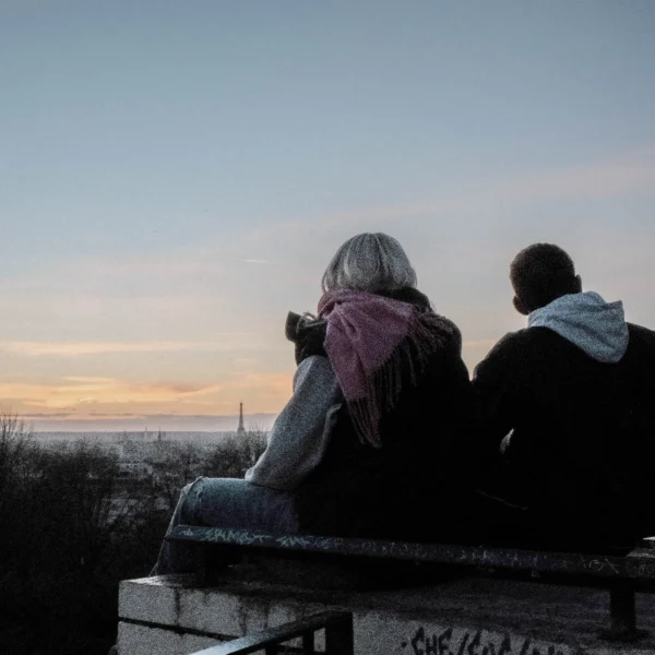Nathalie F. · 07/02/2026 · 4160 x 4160 Cette photographie capture deux personnes assises sur un rebord, dos à l'appareil. Le sujet principal est leur silhouette, avec une attention particulière sur la personne de gauche qui semble observer ou photographier le paysage.La composition est simple et épurée, avec un cadrage serré sur les deux individus et un arrière-plan dégagé montrant un horizon lointain. La lumière, douce et tamisée, suggère un coucher de soleil, créant une ambiance paisible et mélancolique. Les couleurs dominantes sont les teintes bleutées et orangées du ciel crépusculaire, contrastant avec les tons neutres des vêtements.Le style est réaliste et naturel, évoquant une ambiance contemplative et intime.