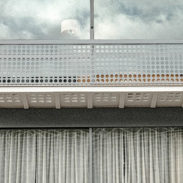 Nathalie F. · 21/02/2026 · 4160 x 4160 Cette photographie met en scène une structure architecturale moderne avec un **sujet principal** : une balustrade ajourée en béton blanc et des éléments en métal. La **composition** est épurée, avec un cadrage serré sur les détails géométriques et les motifs répétitifs. La **lumière**, naturelle et diffuse, crée des contrastes doux entre ombres et clartés.Les **couleurs dominantes** sont le gris, le blanc et des touches de rouille. Le **style** est minimaliste et industriel, évoquant une esthétique contemporaine. L’**ambiance** est sobre et presque austère, renforcée par le ciel nuageux en arrière-plan.