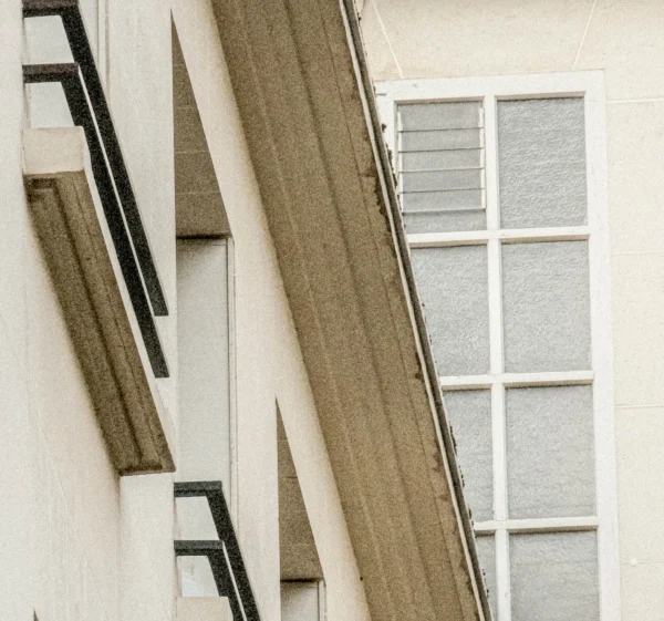 Nathalie F. · 2404 x 2248 Cette photographie met en scène une partie d’un bâtiment moderne. Le sujet principal est l’architecture géométrique, avec des lignes anguleuses et des panneaux en bois clair contrastant avec des surfaces blanches et des fenêtres à carreaux gris.La composition joue sur les diagonales et les contrastes de formes. Le cadrage serré accentue les détails architecturaux. La lumière semble naturelle, douce et légèrement diffuse, créant des ombres subtiles.Les couleurs dominantes sont le blanc, le gris et le bois naturel, donnant un style épuré et contemporain. L’ambiance est minimaliste et élégante, évoquant la modernité et la sobriété.