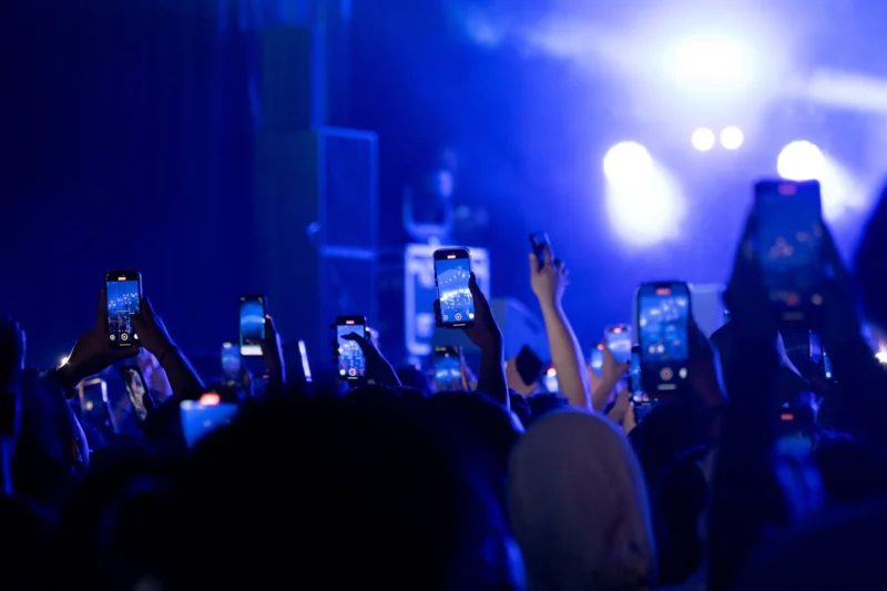 Daniel · 4293 x 2862 Cette photographie capture une scène de concert. Le sujet principal est le public, dont les mains et smartphones sont visibles, filmant ou prenant des photos de la scène. La composition montre une foule dense, avec un cadrage serré sur les bras levés.Les lumières bleutées et les éclairages de scène dominent, créant une ambiance énergique et nocturne. Les couleurs principales sont des teintes froides (bleu, violet) avec des éclats lumineux. Le style est dynamique et moderne, reflétant l'excitation d'un événement musical. L'ambiance est électrique, typique d'un concert en plein air ou en salle.