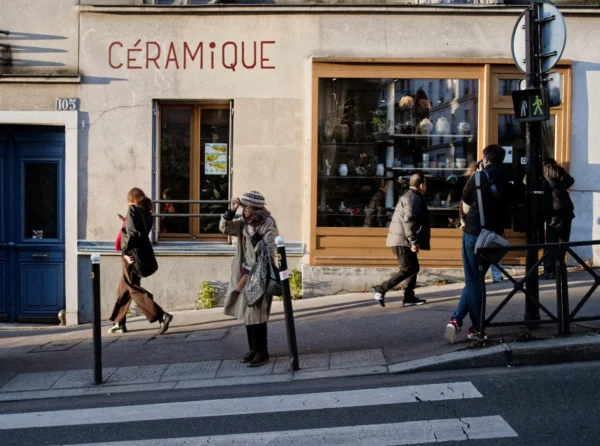 Cyrille · 2026 x 1507 Cette photographie capture une scène urbaine devant une boutique nommée **« Céramique »**. Le sujet principal est un groupe de personnes en mouvement, traversant la rue.La composition est dynamique, avec un cadrage en plan moyen. Les passants sont disposés en diagonale, créant un effet de profondeur. La lumière est naturelle, probablement en journée, avec des ombres douces. Les couleurs dominantes sont neutres (beige, gris) avec des touches de bleu et de vert.Le style est documentaire, réaliste, reflétant une ambiance quotidienne et animée d’une rue parisienne.