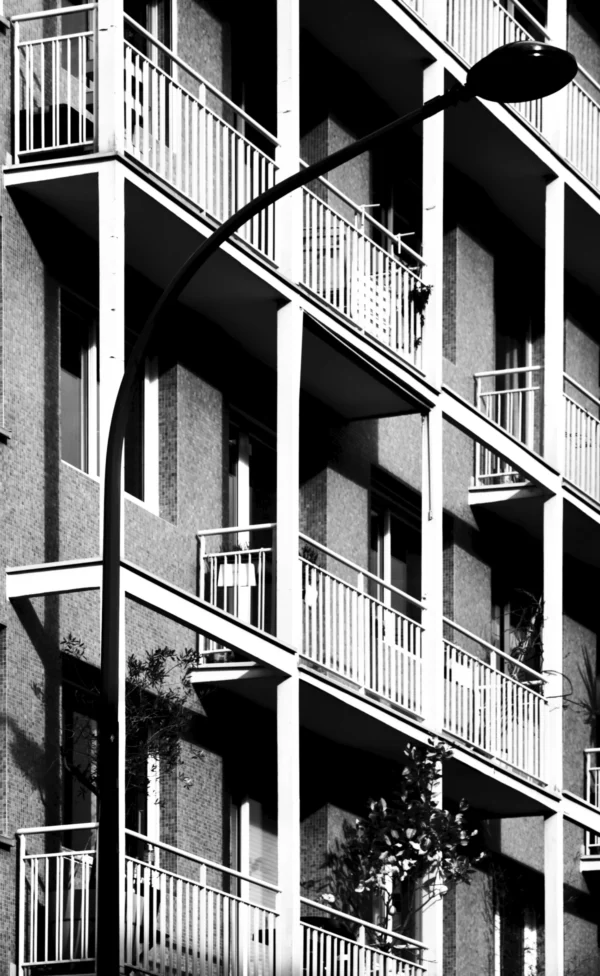 Thomas · 21/02/2026 · 2048 x 3331 Cette photographie en noir et blanc met en scène un immeuble résidentiel avec des balcons en fer forgé. Le sujet principal est l’architecture et les détails des balcons, dont certains sont ornés de plantes et d’objets.La composition est verticale, mettant en valeur la hauteur de l’immeuble. Le cadrage est serré, capturant plusieurs étages. La lumière, naturelle et contrastée, accentue les ombres et les textures métalliques. Les couleurs, limitées au noir et blanc, renforcent les contrastes et les jeux de lumière.Le style est documentaire et esthétique, évoquant une ambiance urbaine et intemporelle.