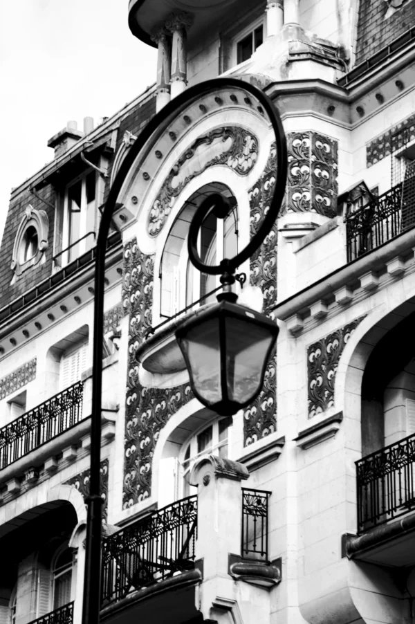 Thomas · 21/02/2026 · 2048 x 3080 Cette photographie en noir et blanc met en valeur une façade architecturale élégante. Le sujet principal est une lanterne murale ornée, intégrée à une structure ornementée de motifs géométriques et végétaux. La composition est verticale, avec un cadrage serré qui accentue les détails architecturaux.La lumière, douce et contrastée, souligne les textures et les reliefs. Les tons dominants varient du blanc au gris foncé, créant une ambiance à la fois classique et mystérieuse. Le style rappelle l’art nouveau ou l’architecture haussmannienne, évoquant une élégance intemporelle et un charme historique.