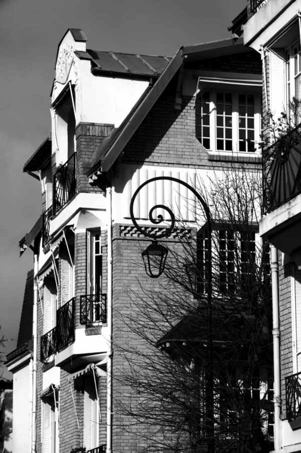 Thomas · 21/02/2026 · 2048 x 3080 Cette photographie en noir et blanc met en scène un immeuble résidentiel ancien. Le sujet principal est la façade, marquée par des détails architecturaux comme les balcons en fer forgé et les fenêtres. La composition est verticale, avec un cadrage serré sur la partie supérieure du bâtiment, accentuant les lignes et les textures.La lumière, tamisée, crée des contrastes entre ombres et clartés, soulignant les reliefs. Les couleurs dominantes, bien que monochromes, varient du noir profond au gris clair. Le style est documentaire et esthétique, évoquant une ambiance mélancolique et intemporelle, renforcée par l'absence de végétation dense et les éléments architecturaux vieillissants.