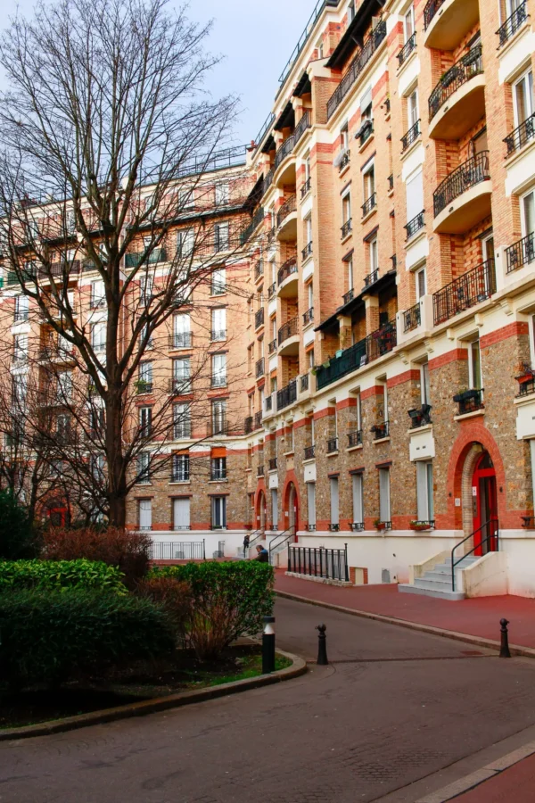 Cédric · 1365 x 2048 Cette photographie montre un immeuble parisien typique, sujet principal. La composition met en valeur une façade élégante avec balcons en fer forgé et détails architecturaux classiques. Le cadrage est serré, centré sur l'entrée et les étages supérieurs.La lumière est douce et naturelle, probablement en fin de journée, créant une ambiance tamisée. Les couleurs dominantes sont les tons neutres (beige, gris) rehaussés par des touches de rouge et vert. Le style est urbain et traditionnel, évoquant une ambiance calme et résidentielle, typique des quartiers historiques parisiens.