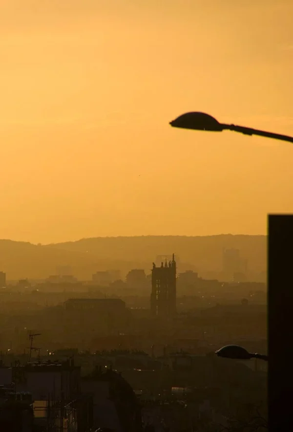 Pascale · 679 x 1000 Cette photographie capture un coucher de soleil urbain. Le sujet principal est une silhouette floue de bâtiments et de collines baignés dans une lumière dorée. La composition inclut une lampe de rue en premier plan, encadrée par des éléments architecturaux sombres.Le cadrage est serré, mettant en valeur les contours et les ombres. La lumière douce et diffuse crée une ambiance chaleureuse et apaisante. Les couleurs dominantes sont des tons chauds de jaune, orange et brun, avec des contrastes subtils entre les ombres et les lumières.Le style est épuré et atmosphérique, évoquant une sensation de tranquillité et de mélancolie.
