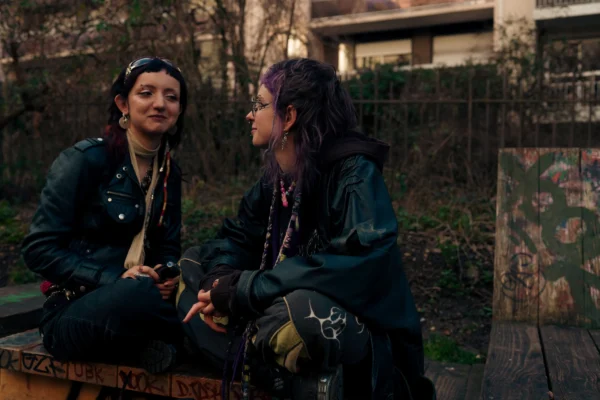 Don · 6549 x 4366 Cette photographie met en scène deux jeunes femmes assises sur un banc, engagées dans une conversation. Le sujet principal est leur interaction, captée en plan serré.La composition est naturelle, avec un cadrage centré sur elles, légèrement en contre-plongée. La lumière est douce et tamisée, typique d’un extérieur en fin de journée ou sous un ciel couvert, créant une ambiance intimiste.Les couleurs dominantes sont les tons neutres (bleu foncé des vestes, vert des arbres) et quelques touches de rouge et noir, renforçant une atmosphère sobre et légèrement mélancolique. Le style est réaliste et documentaire, évoquant une scène du quotidien.