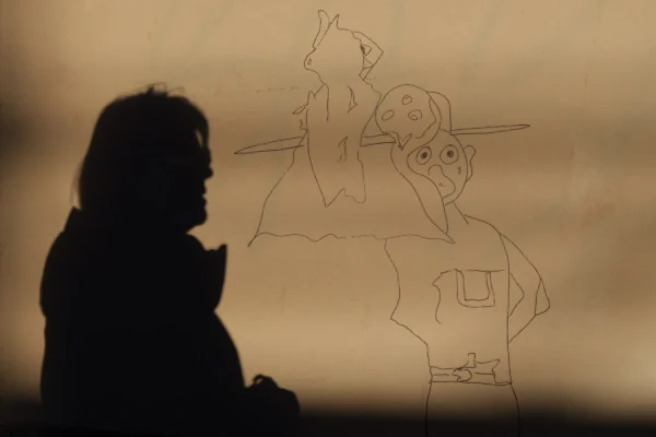 Don · 4469 x 2979 Cette photographie montre une silhouette d’une personne assise devant une projection lumineuse représentant des personnages stylisés, probablement inspirés d’un dessin animé ou d’une bande dessinée.La composition joue sur le contraste entre l’ombre du sujet et la lumière colorée des silhouettes projetées. Le cadrage est serré, mettant en valeur les deux éléments. La lumière douce et tamisée crée une ambiance chaleureuse et onirique. Les couleurs dominantes sont des tons sépia et orangés, renforçant l’aspect nostalgique et artistique. Le style évoque un mélange de réalisme et de fantaisie, évoquant une scène intime et contemplative.