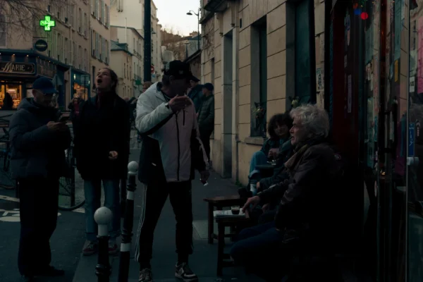 Don · 4218 x 2812 Cette photographie capture une scène urbaine nocturne ou crépusculaire. Le sujet principal semble être un groupe de personnes en interaction, dont une personne debout au premier plan, filmée ou photographiée avec un smartphone.La composition est dynamique, avec des lignes architecturales convergentes et des jeux d'ombres. Le cadrage est serré, mettant en valeur les visages et les attitudes. La lumière, douce et tamisée, crée une ambiance chaleureuse et intimiste, avec des teintes dominées par des tons gris-beige et des reflets dorés.Le style est réaliste et documentaire, évoquant une ambiance authentique et spontanée.